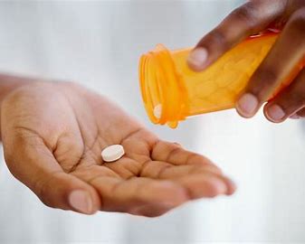 A hand receiving a tablet of Adderall pill from a yellow pill cup